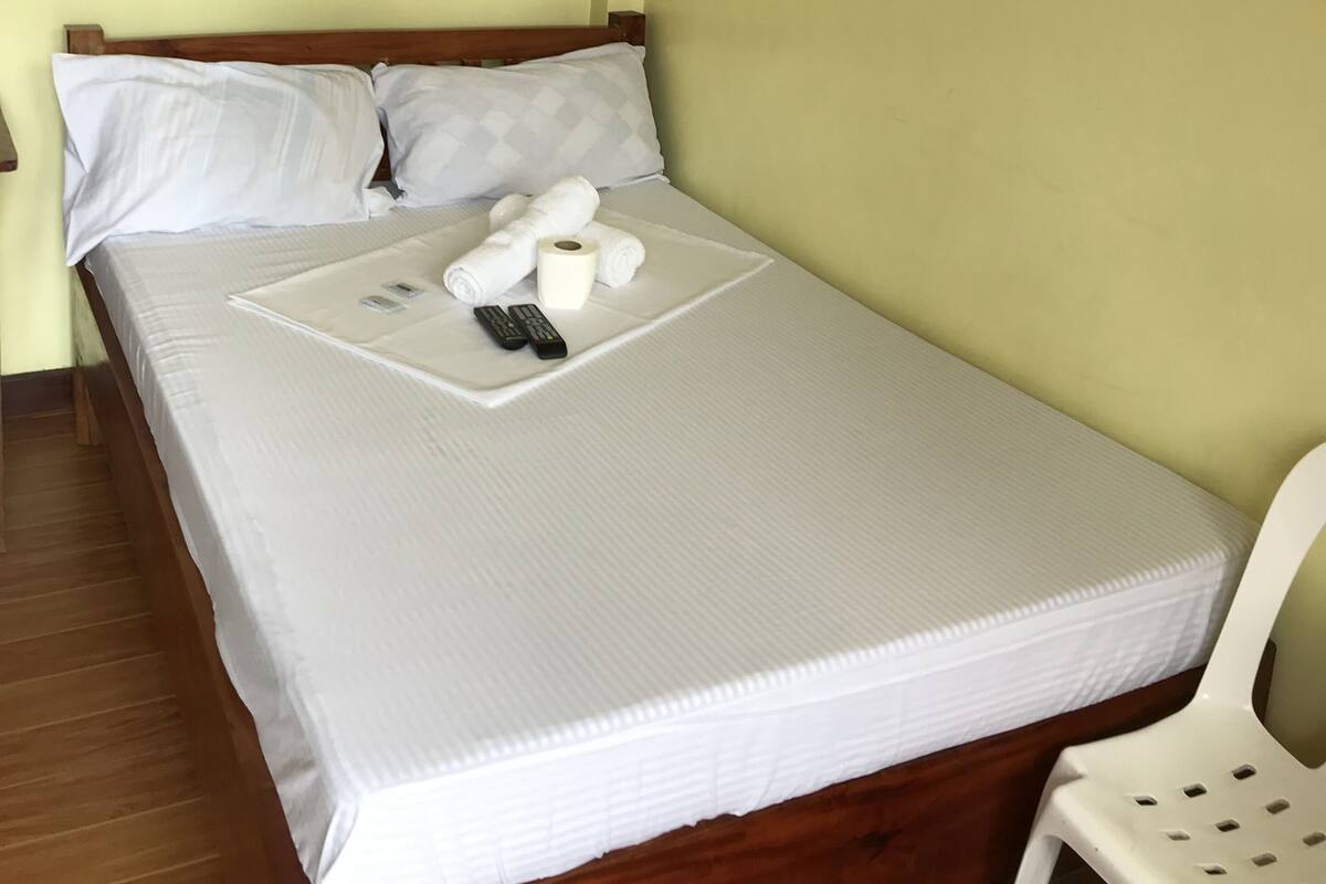A single bed with white bedding, a wooden headboard, and a white chair.