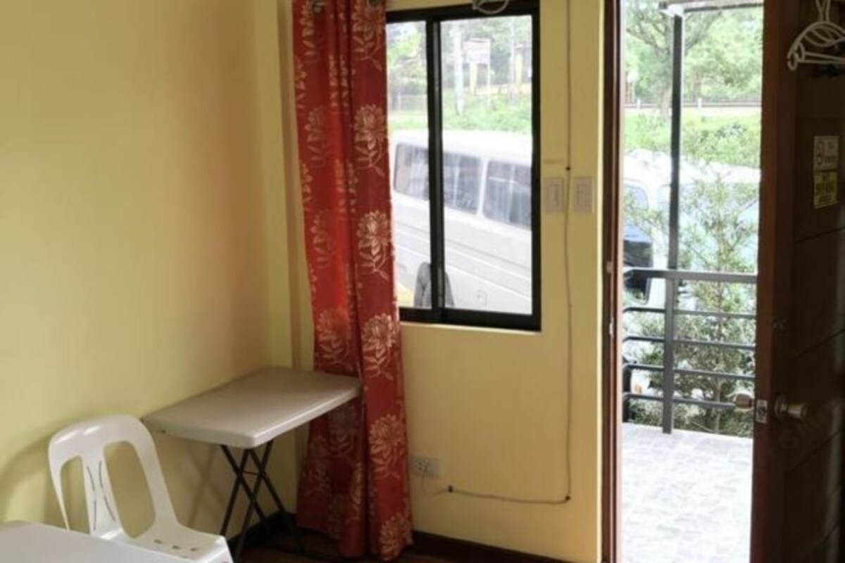 A small room with a window, a white chair, a small table, and a red curtain.