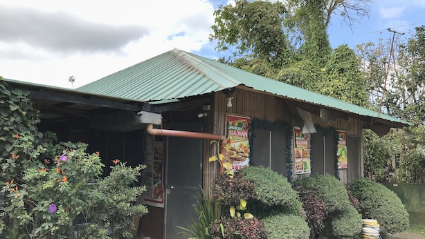 A rustic building with a green roof, surrounded by lush greenery and flowering plants. - Jhunlyn Rooms for Rent Tagaytay (Tagaytay)