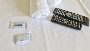 A neatly made bed with two rolled towels, a roll of toilet paper, two remote controls, and two packets of bath soap. - Jhunlyn Rooms for Rent Tagaytay (Tagaytay)
