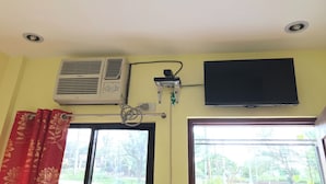A room with a ceiling fan, an air conditioning unit, a television mounted on the wall, and a window with red curtains. - Jhunlyn Rooms for Rent Tagaytay (Tagaytay)