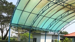 A swimming pool with a covered area and a building in the background. - Sripiamsuk (Pathum Thani)