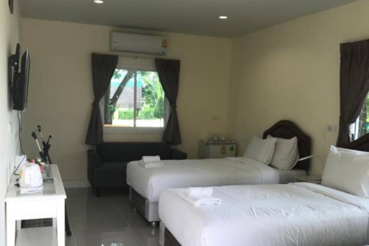 A hotel room with three beds, a TV, a desk, and a window with curtains.