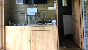 A wooden cabin interior with a kitchenette, a mounted television, a fan, and a refrigerator. - Sripiamsuk (Pathum Thani)