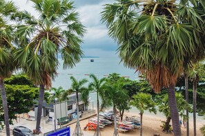 A beach view with palm trees, a boat in the water, and a building with a blue sign. - G.I Lodge by Zuzu (Pattaya)