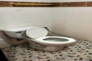 A toilet with a raised seat in a bathroom with patterned floor tiles and a decorative wall border. - G.I Lodge by Zuzu (Pattaya)