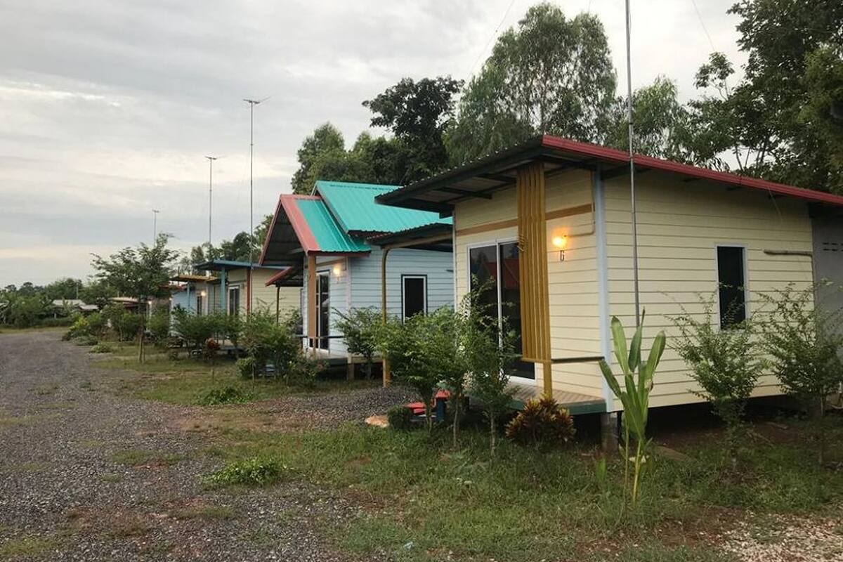 Fileira de casas pequenas, térreo, com calçada de cascalho e vegetação ao redor.