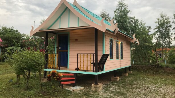 Una casa pequeña de un solo piso con techo inclinado, un porche con banca y el número 19 en la puerta.