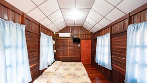 Una habitación con paredes de madera, techo de baldosas, cama con ropa de cama floral y cortinas en las ventanas.