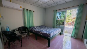 Una habitación con cama, una silla, una mesita y un ventanal con cortinas.