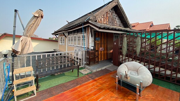 A traditional wooden house with a sloped roof, a wooden bench, a small table, and a white inflatable hot tub. - Center Home City (Chiang Mai)