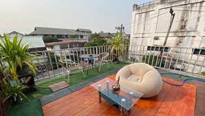 A rooftop patio with a glass coffee table, a beige bean bag, and a small table with chairs. - Center Home City (Chiang Mai)