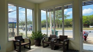 A waiting area with large windows, a potted plant, and wooden chairs. - Andaman Place (Thep Krasattri)