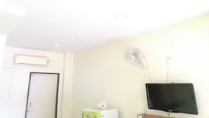 A room with a white ceiling, a white door, a white air conditioner, a white fan, and a black TV mounted on the wall. - Andaman Place (Thep Krasattri)