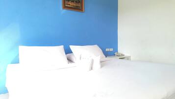 A bed with white bedding and pillows, a nightstand with a phone, and a framed picture on the wall.