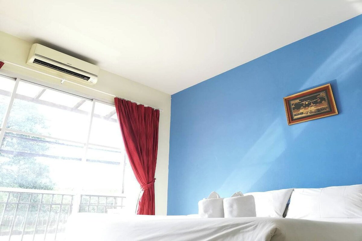 Ein Hotelzimmer mit einem Bett, einem Fenster mit roten Vorhängen, einer Klimaanlage und einem gerahmten Bild an der Wand.