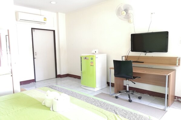 Habitación de hotel con cama, escritorio con silla, televisor, refrigerador y ventilador.