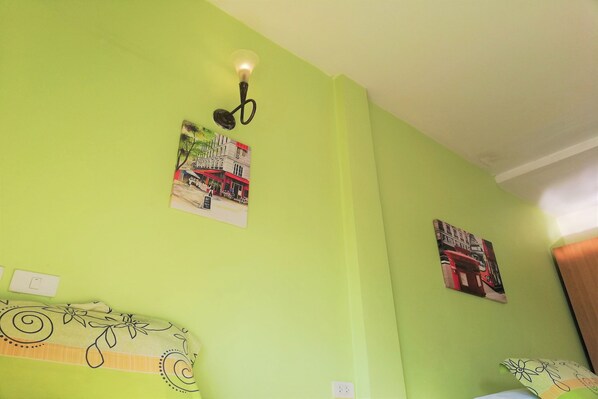 Una habitación con paredes verdes, una cama con colcha estampada y una lámpara de pared, junto con dos cuadros enmarcados.