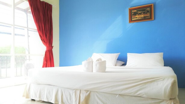 A bed with white bedding, a red curtain, and a framed picture on a blue wall. - Andaman Place (Thep Krasattri)