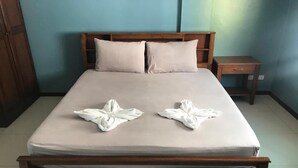 A neatly made bed with two towels folded into flower shapes, a wooden headboard, a nightstand, and a blue wall. - JT Guesthouse (Kamala)