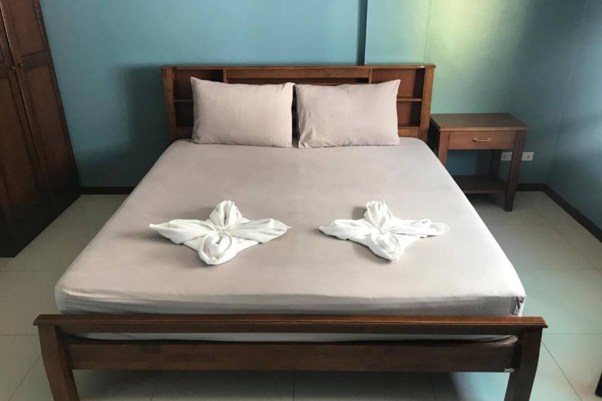 A neatly made bed with two towels folded into flower shapes, a wooden headboard, a nightstand, and a blue wall.