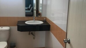 A compact bathroom with a white toilet, a black sink with a mirror above it, and a door to the right. - JT Guesthouse (Kamala)