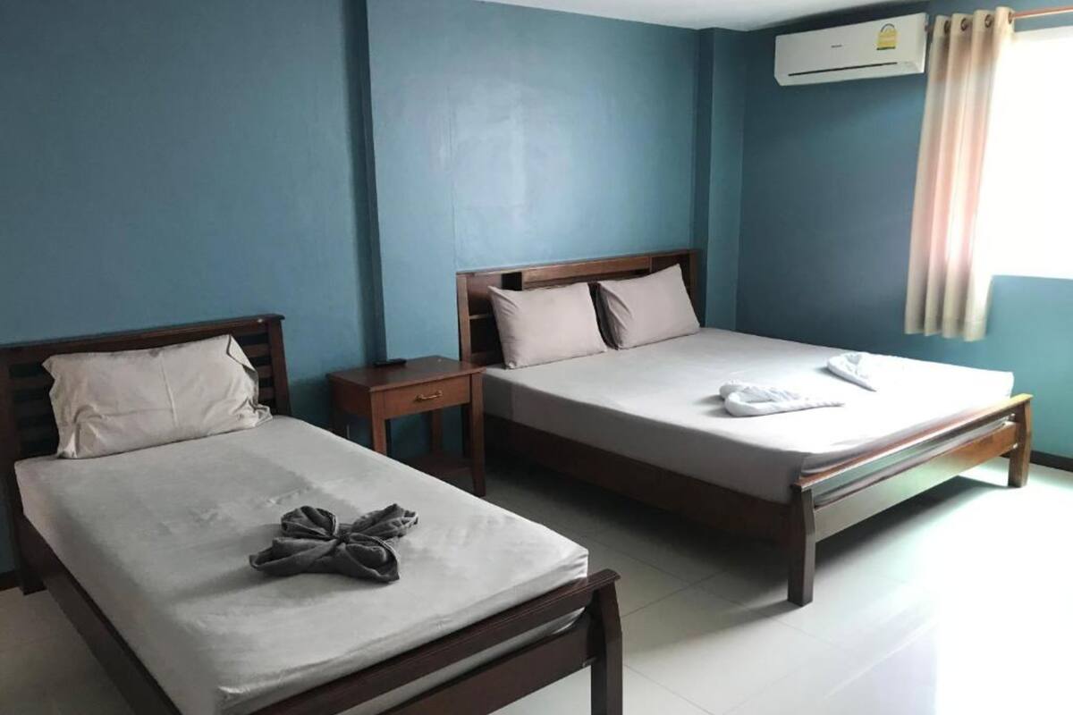 Two single beds with wooden frames and white linens in a room with blue walls and a tiled floor.