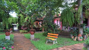 A garden pathway leading to a building with a red roof, surrounded by lush greenery and a bench. - Euangnuae Resort (Mae Rim)