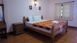 A bedroom with a wooden bed, white pillows, a checkered blanket, a nightstand, a dresser, a wall-mounted lamp, and a window with striped curtains. - Euangnuae Resort (Mae Rim)