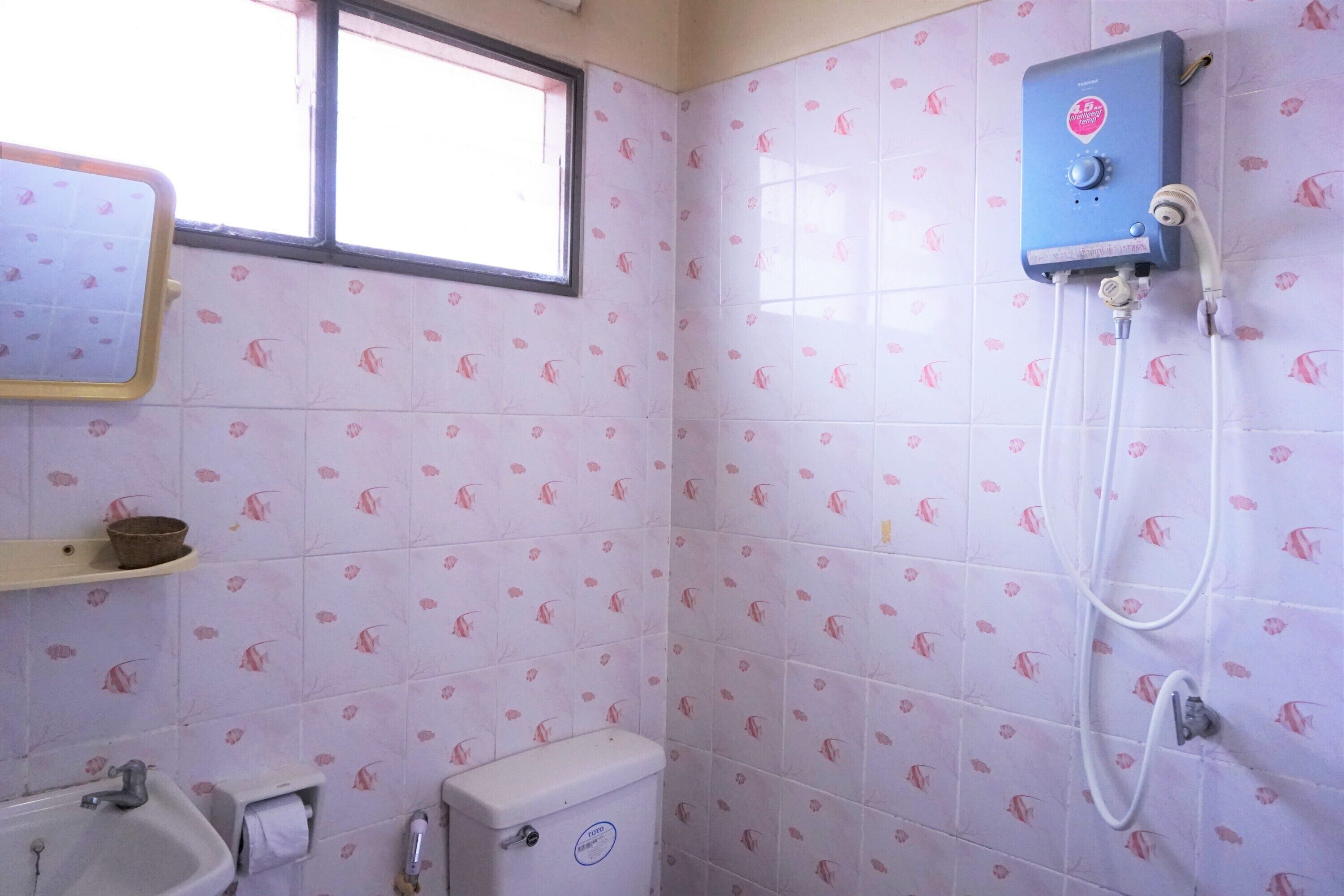 Une salle de bain avec des carreaux roses ornés de motifs de poissons, des toilettes, un lavabo et une douche.