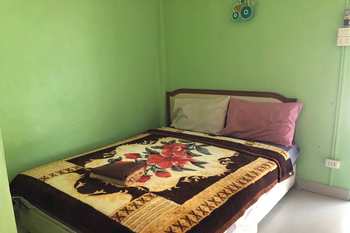 A bed with a floral-patterned bedspread, a brown blanket, and a brown pillow.