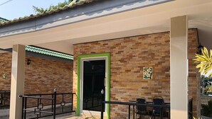 A building with a brick facade, a green-framed entrance, and outdoor seating with metal railings. - Romsai Resort (Bang Lamung)