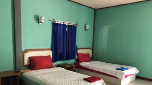 A hotel room with two single beds, each with a red pillow and a white bedspread. There are two nightstands, one with a lamp on each side of the beds. The room has teal walls and a window with blue curtains. - Romsai Resort (Bang Lamung)