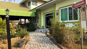 A building with a green exterior, a stone pathway leading to the entrance, and a sign indicating the name. - Romsai Resort (Bang Lamung)