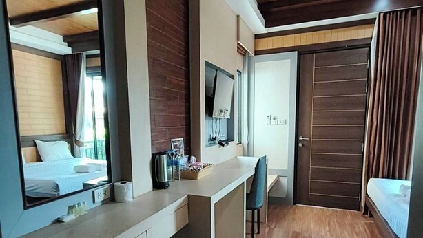 A modern hotel room with a wooden ceiling, a large mirror, a desk with a chair, a bed, and a wardrobe. - Thalang Resort (Si Sunthon)