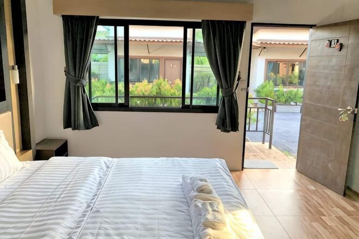 A bedroom with a bed, curtains, a window, and an open door leading to an outdoor area.