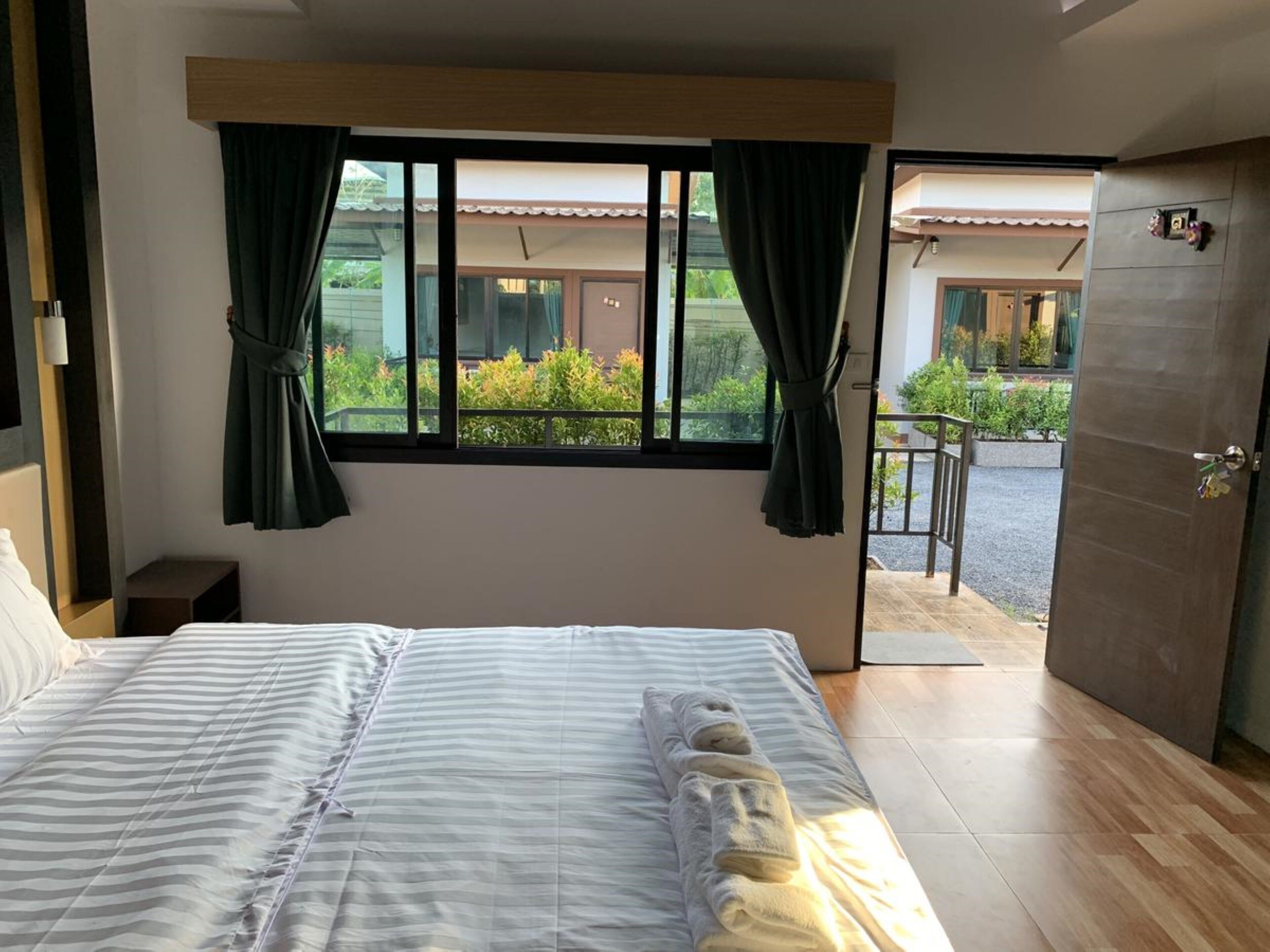 A bedroom with a bed, a window with curtains, and a view of a garden and building outside.