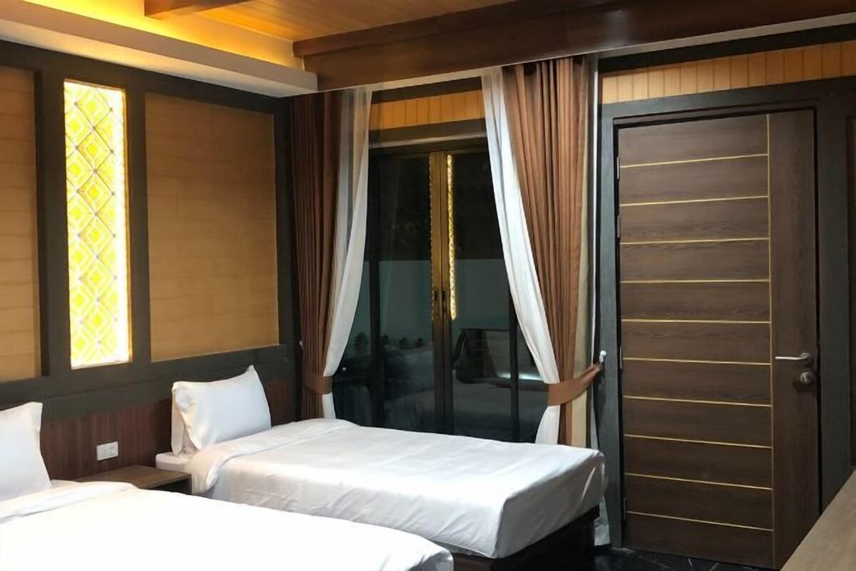 Habitación de hotel con dos camas, una puerta corrediza de vidrio y un armario de madera oscura.