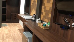 A modern kitchen with wooden cabinets, a built-in oven, a microwave, and a sink. There is a small refrigerator and a basket of snacks on the counter. - Thalang Resort (Si Sunthon)