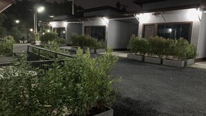 A parking area with multiple buildings, each with a door and windows, surrounded by planters with greenery. - Thalang Resort (Si Sunthon)