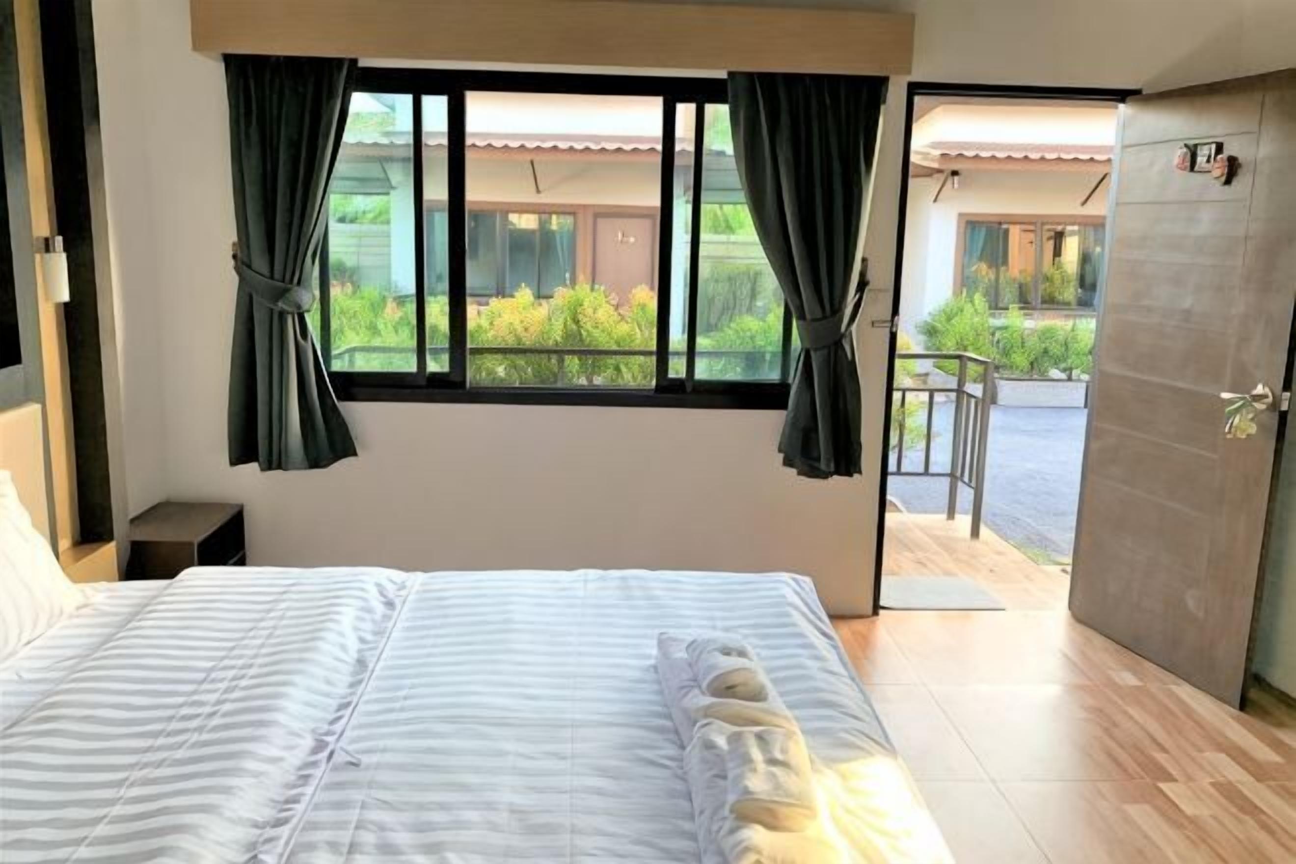 A bedroom with a bed, a window with curtains, a door, and a view of a balcony.