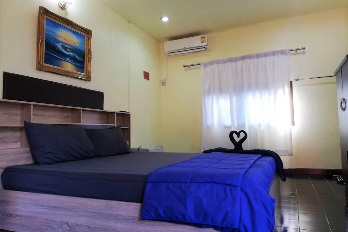 Une chambre à coucher comprenant un lit, une tête de lit, un tableau, un appareil de climatisation et une fenêtre avec des rideaux.