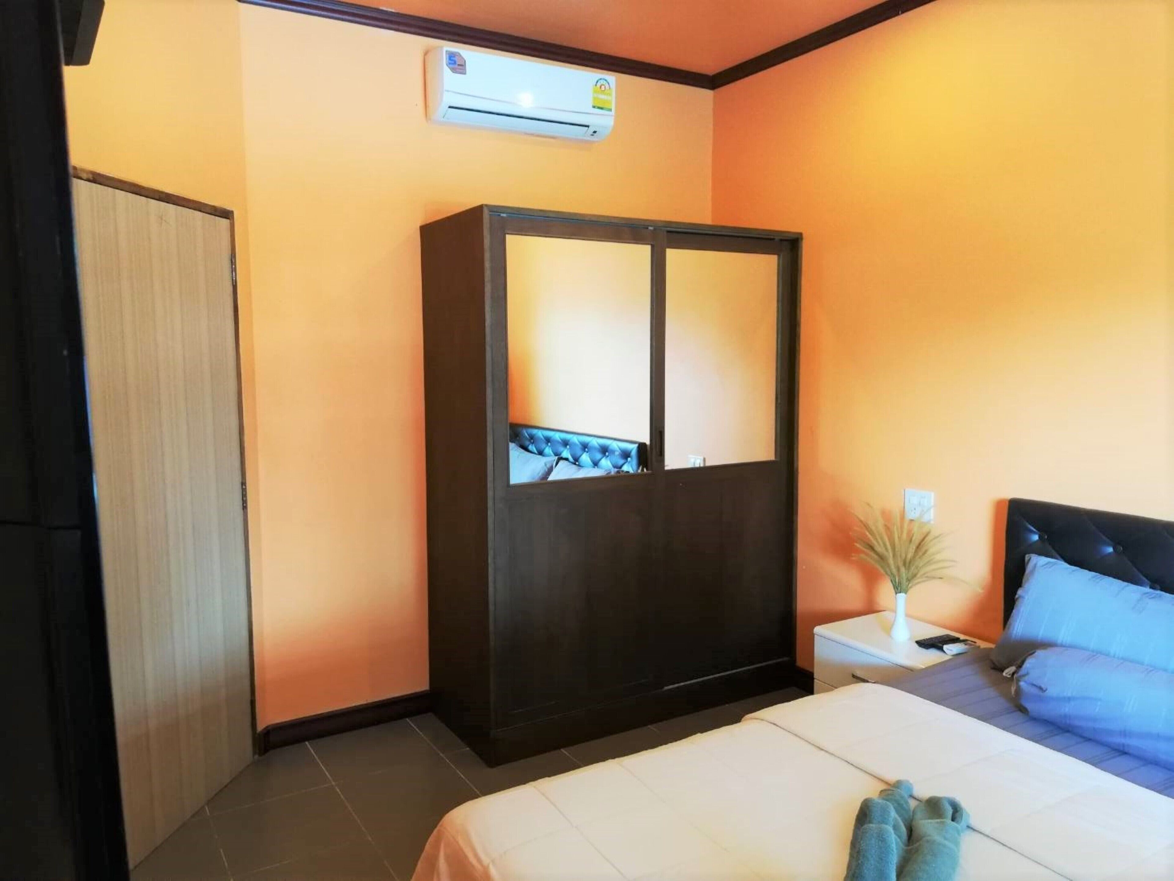 A hotel room with a bed, a wardrobe, a bedside table, and an air conditioning unit.
