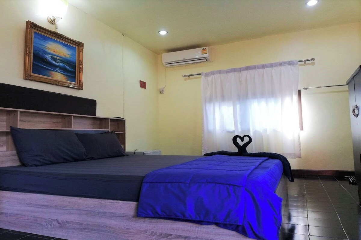 Un dormitorio con cama, cabecera, un cuadro, aire acondicionado y cortina.