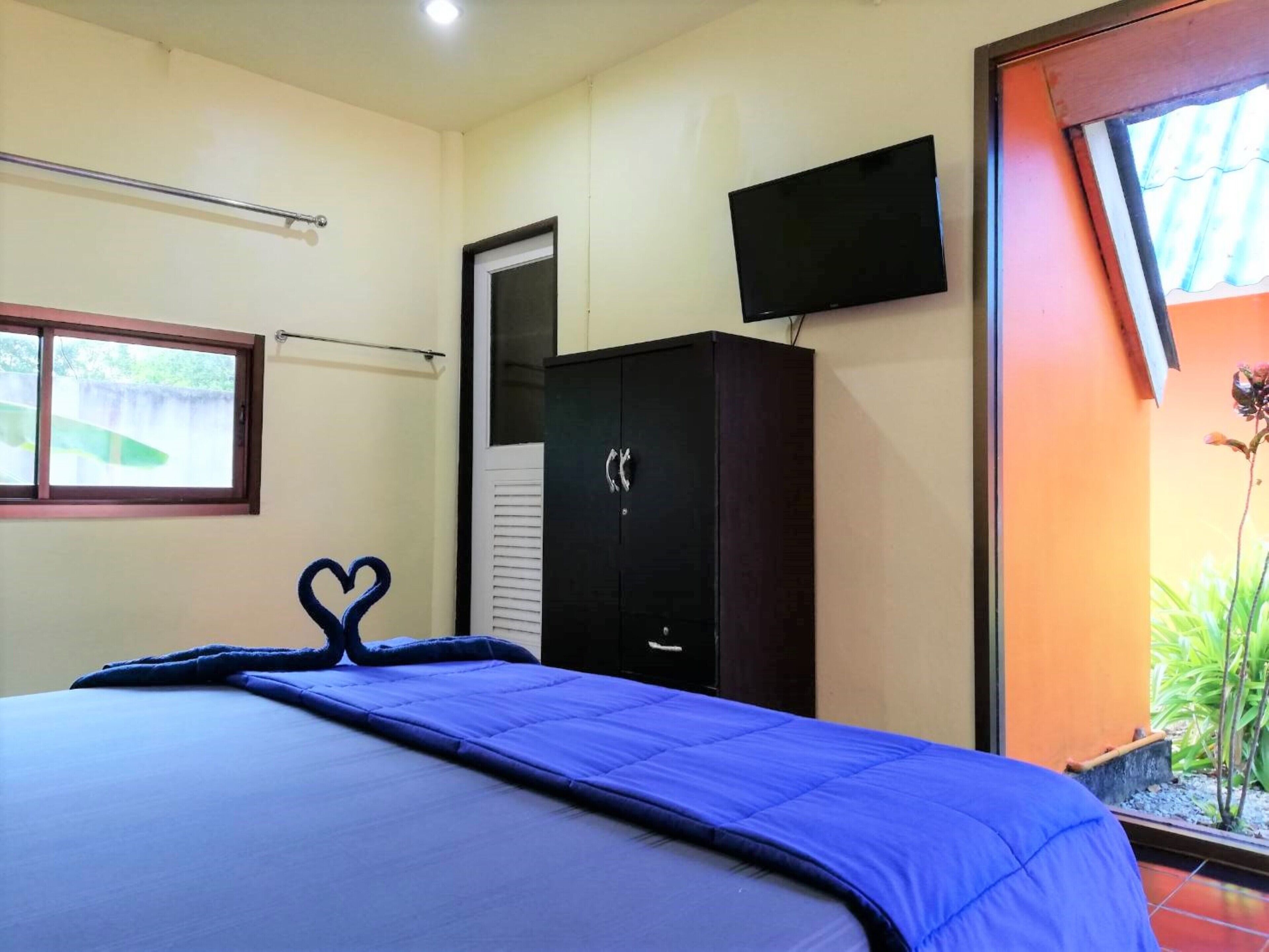 Un dormitorio con cama, armario, televisor y ventana con vistas a zonas verdes.