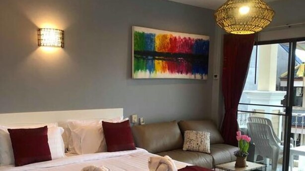 Una habitación de hotel moderna con una cama grande, un sofá, un balcón con vistas y un cuadro abstracto colorido en la pared.