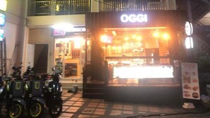 Un edificio de dos pisos con un restaurante llamado 'OGGI' en la planta baja. Hay motocicletas estacionadas afuera.