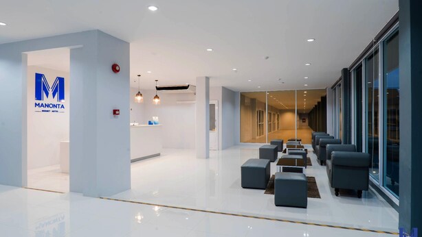 A modern hotel lobby with a reception desk, seating area, and a glass wall offering views of the interior. - Manonta Budget Hotel (Hat Yai)