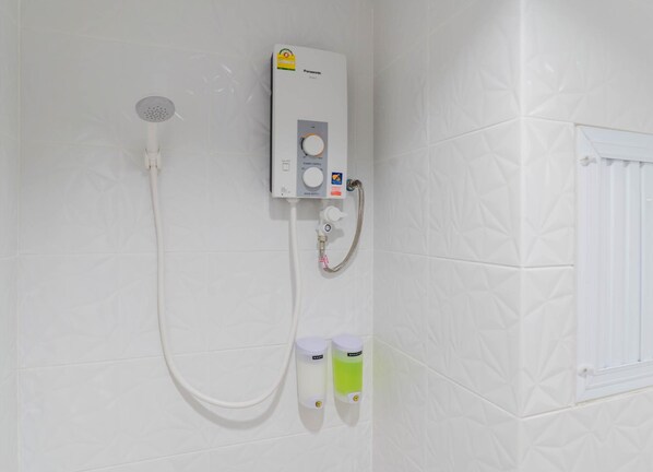 A bathroom with a wall-mounted shower unit, a handheld showerhead, and two soap dispensers. - Manonta Budget Hotel (Hat Yai)