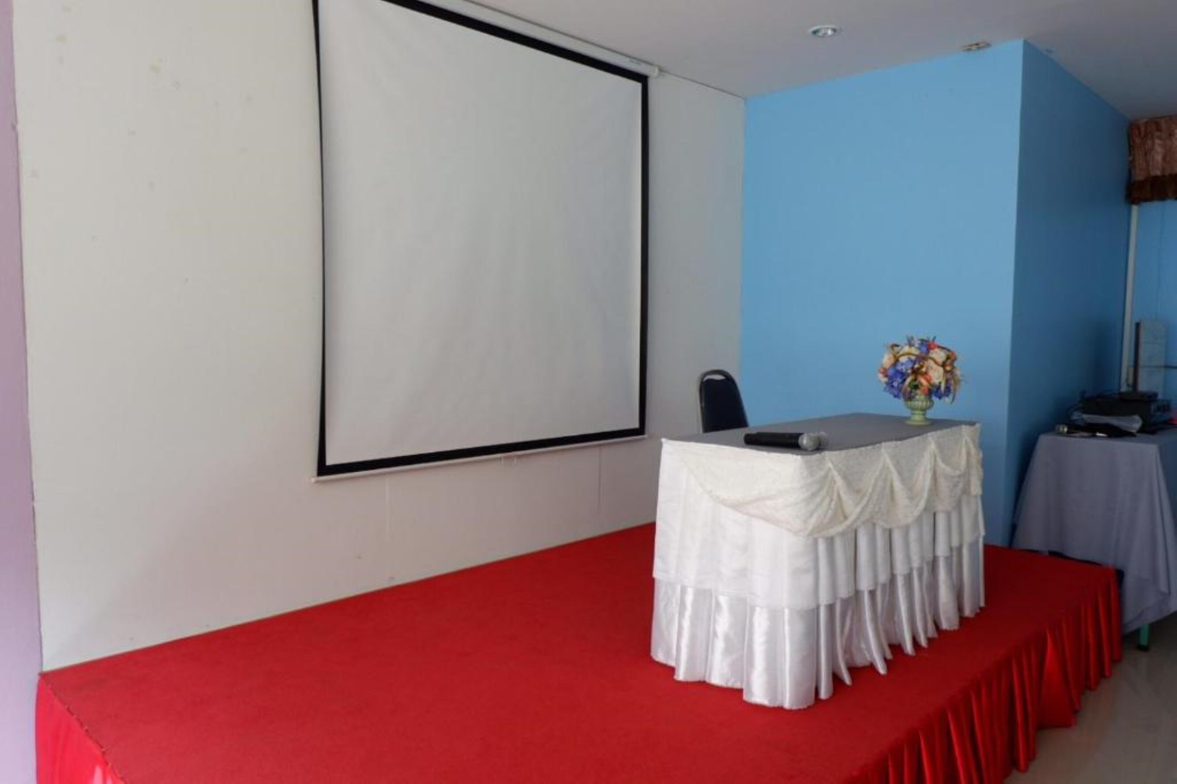Una sala conferenze con un grande schermo, un tavolo bianco con tovaglia rossa e una parete blu.